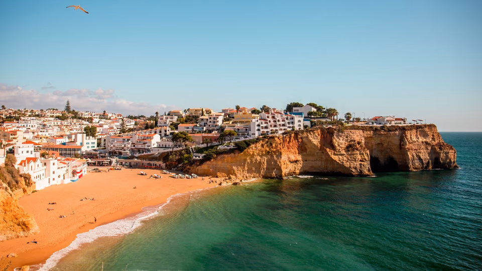 Sandstrand und Felsküste an der Algarve mit weißen Häusern über dem türkisfarbenen Meer